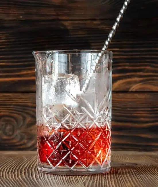 Stirring Negroni ingredients and ice in mixing glass on table