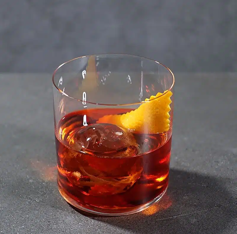Negroni cocktail on large ice cube with orange peel twist