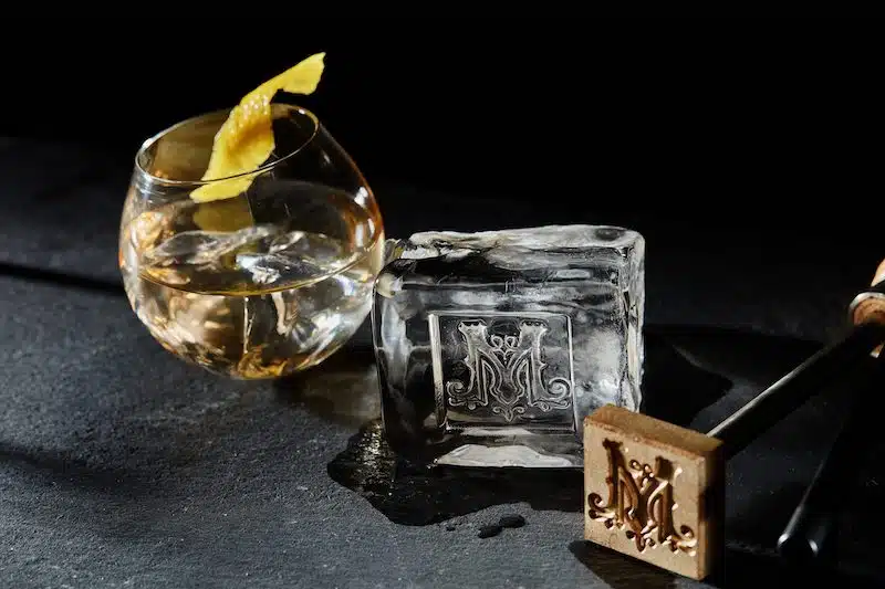 Branded Ice cube next to ice stamp and cocktail