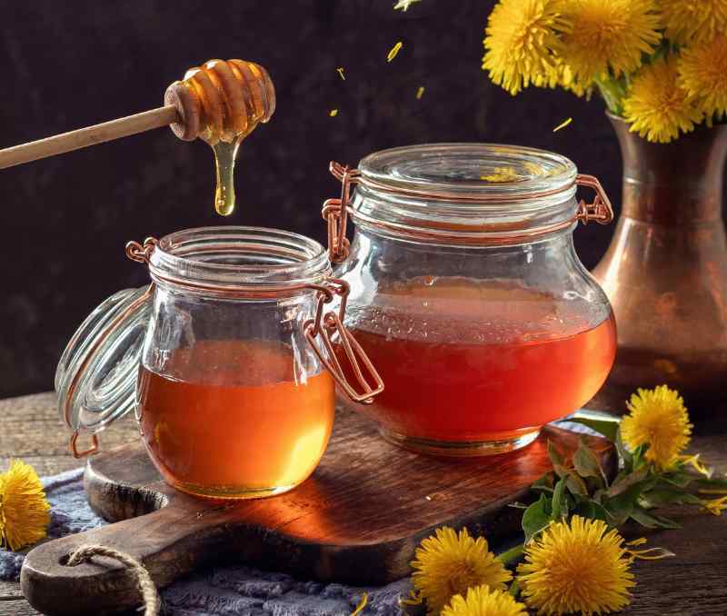 Dandelion honey mix in jars on table with fresh dandelions