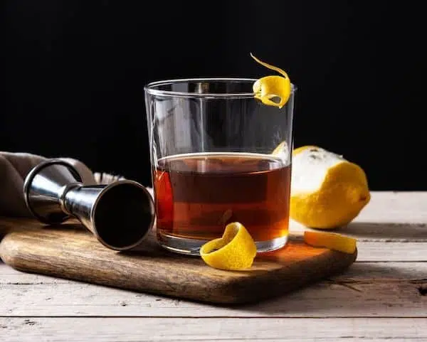 Sazerac Cocktail with lemon peel twist next to lemon on wooden board