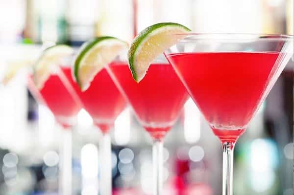 Four Cosmopolitan drinks in Martini garnished with lime wedges