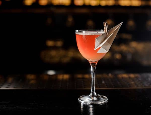 Paper Plane Cocktail on bar counter garnished with small paper plane