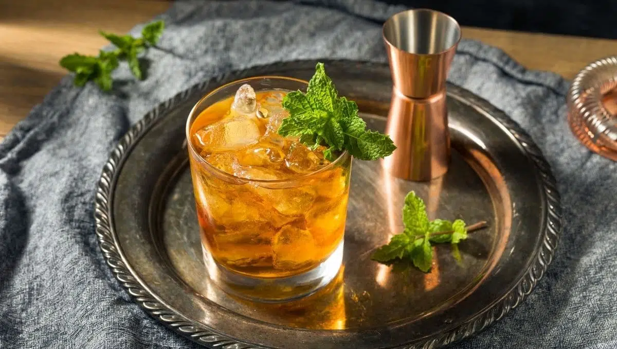 Stinger cocktail on silver tray garnished with mint; next to jigger