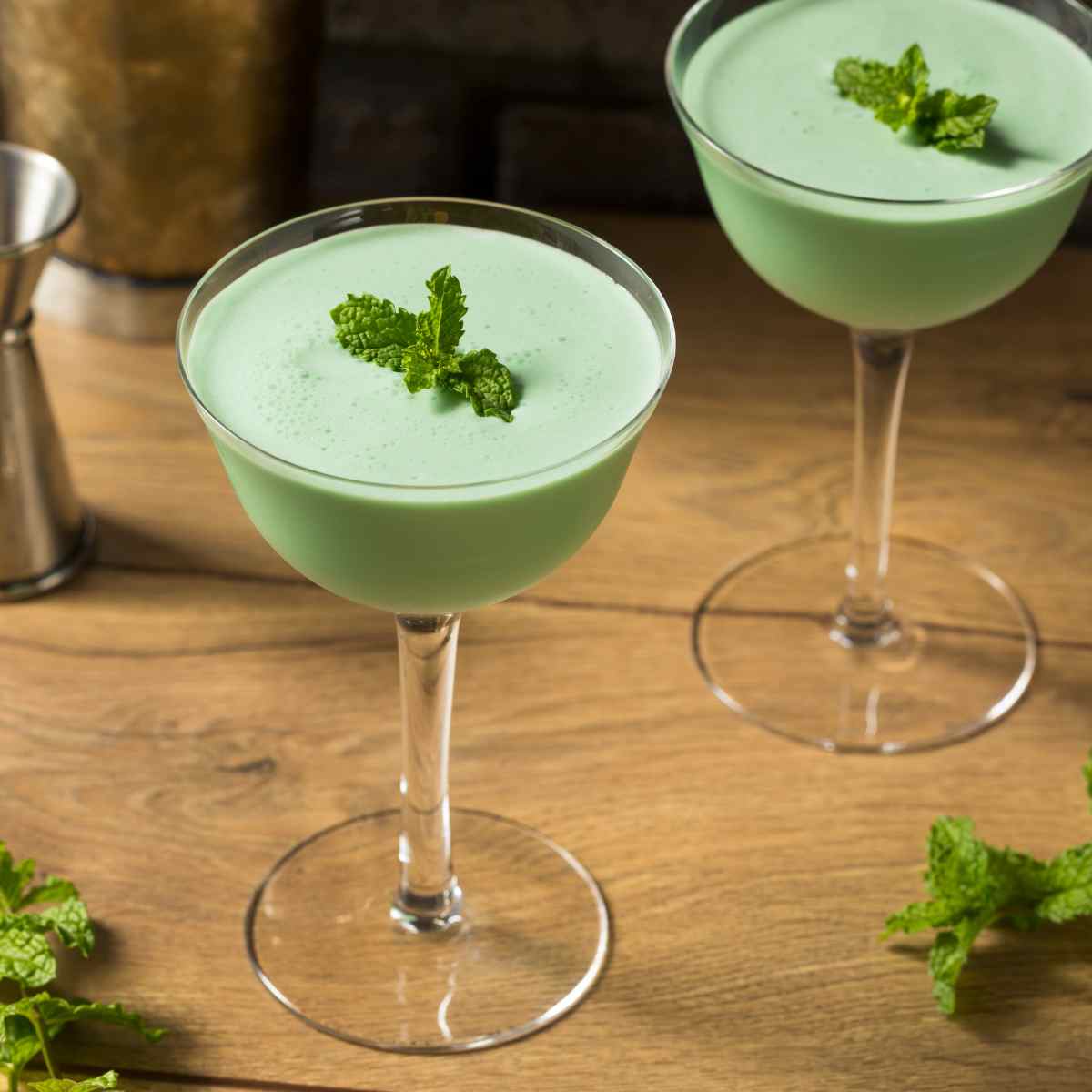 Two Crème de Menthe cocktails on wooden table next to fresh mint leaves