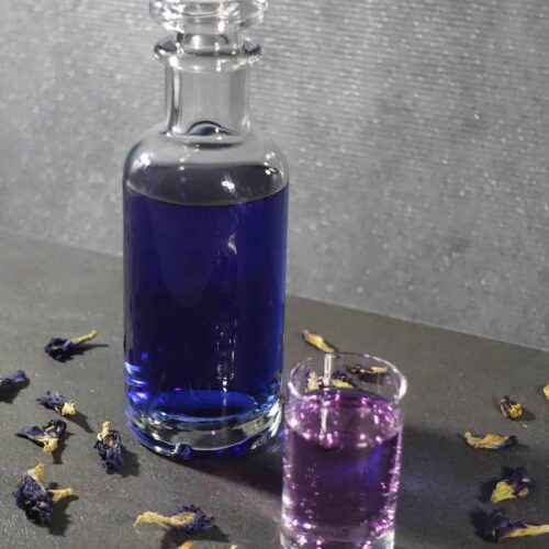 Butterfly Pea Flower infused Gin with flowers and color changing drink in shot glass